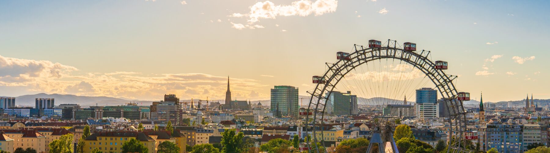 View of Vienna - in the foreground the Prater with the ferris wheel. Behind St. Stephen's Cathedral, skyscrapers, and hills.